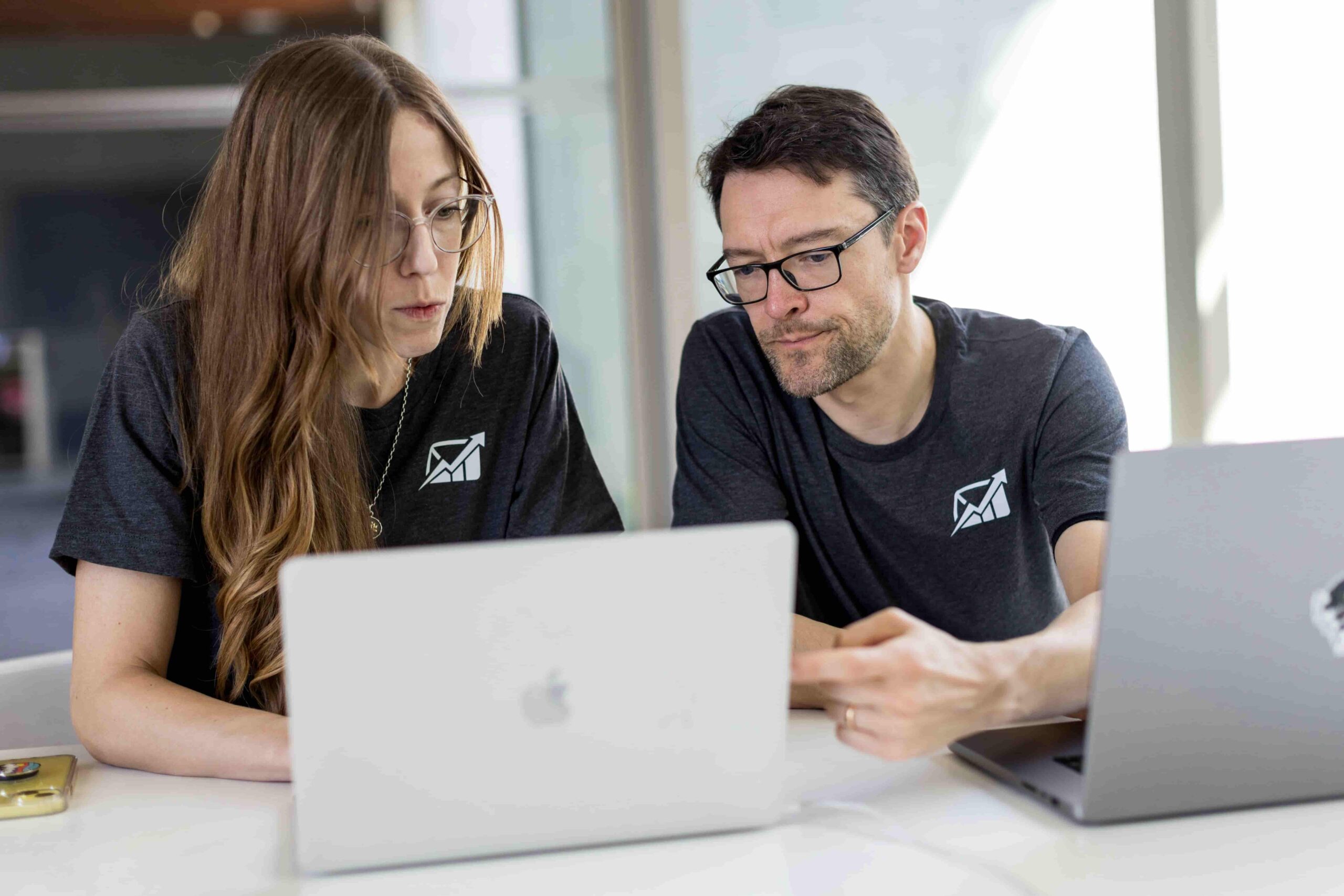 Two IT professionals discussing a project while working on laptops, emphasizing the importance of updated operating systems for business productivity and cybersecurity.